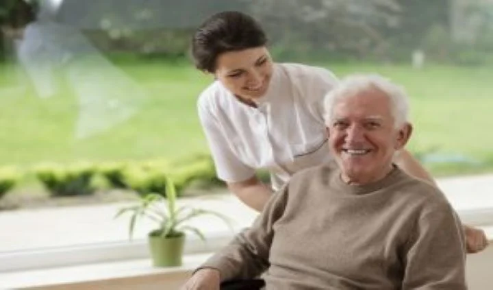 Care worker assisting an older adult seated in a garden